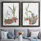 Set of two black barnwood framed canvas prints depicting paired whimsical botanical animal illustrations with curious felines, terracotta pots, succulents, and leafy stems above a sofa in a contemporary living room.