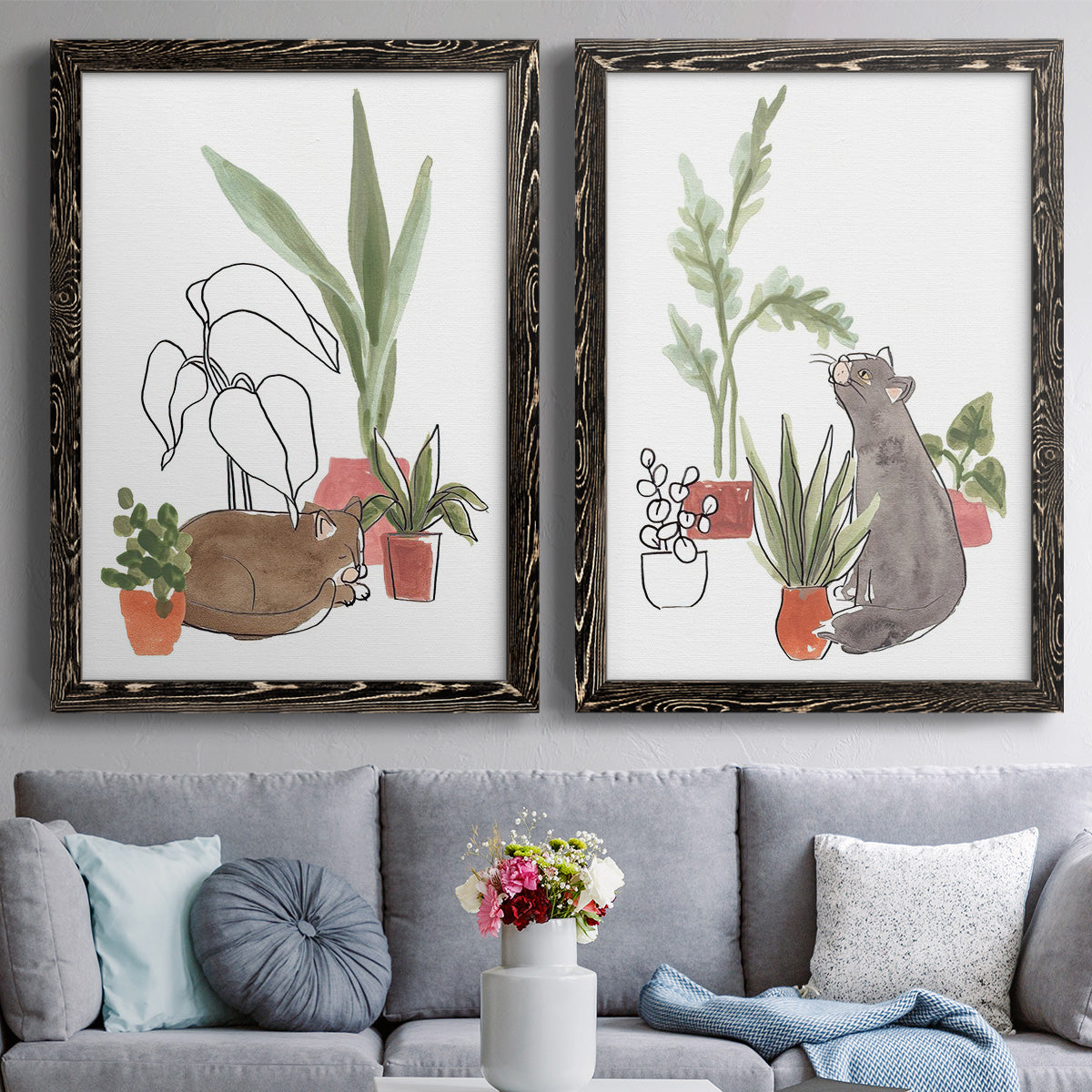 Set of two black barnwood framed canvas prints depicting paired whimsical botanical animal illustrations with curious felines, terracotta pots, succulents, and leafy stems above a sofa in a contemporary living room.
