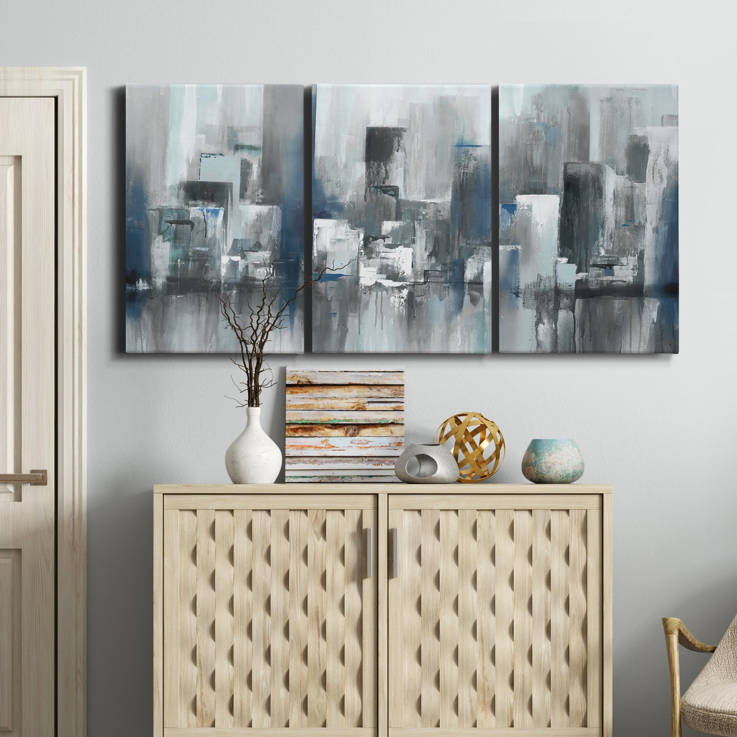 Three-panel canvas wall art featuring urban cityscape rendered in blue tones, displayed above a cabinet in an entryway.