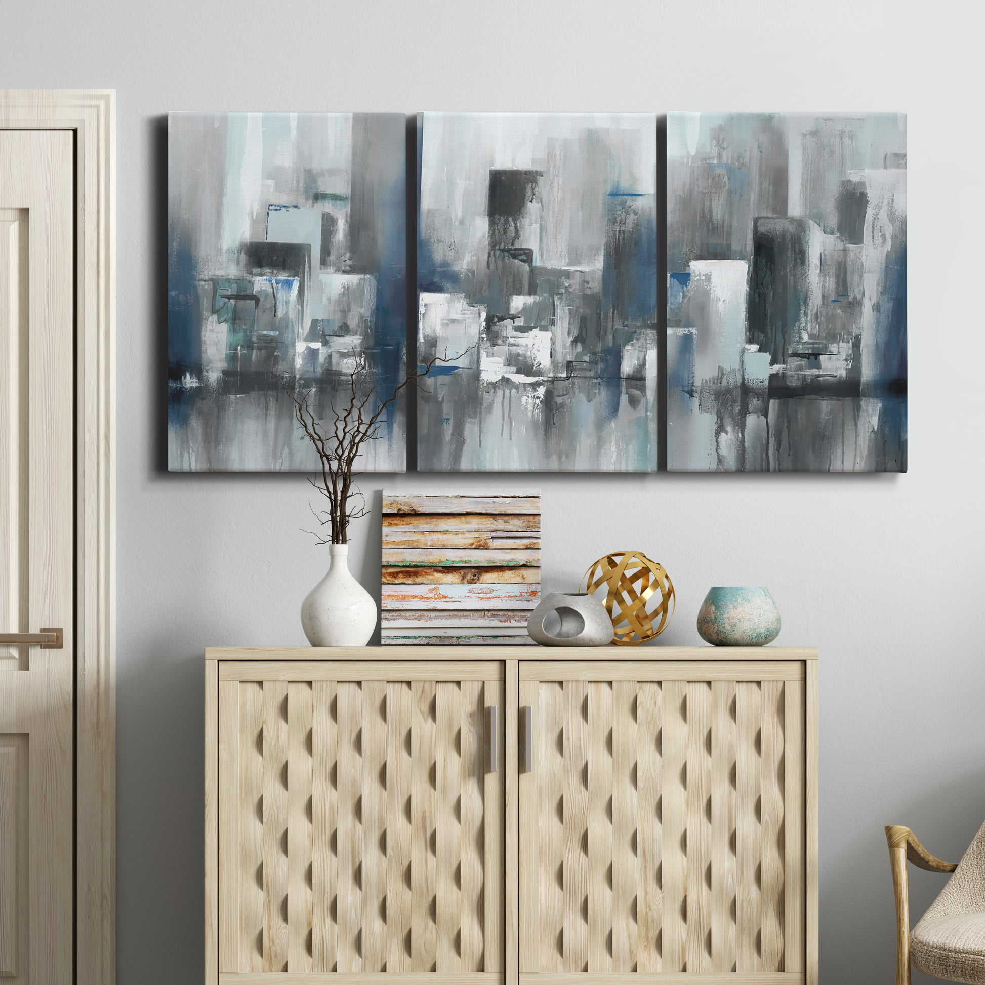 Three-panel canvas wall art featuring urban cityscape rendered in blue tones, displayed above a cabinet in an entryway.