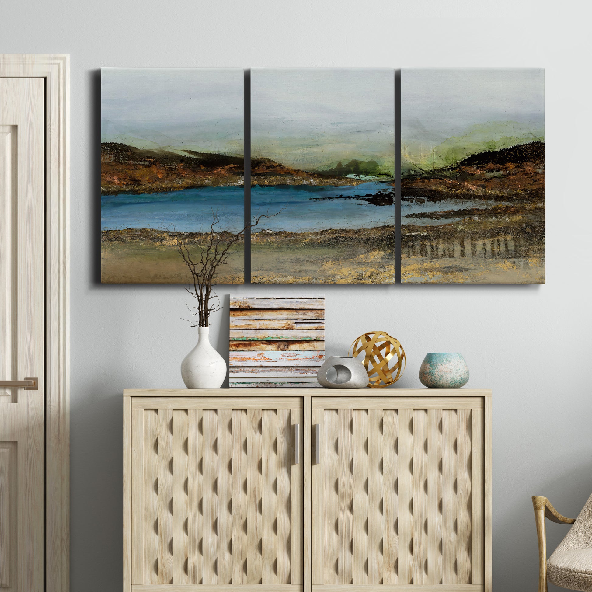 Three-panel canvas wall art featuring peaceful lakeside shoreline landscape, displayed above a cabinet in an entryway.