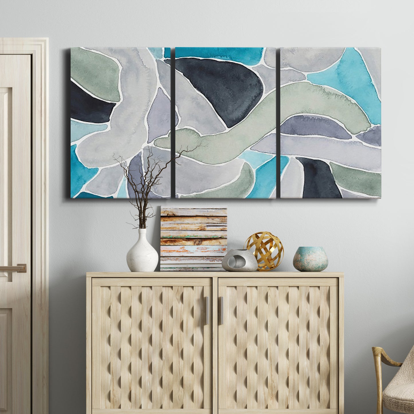 Three-panel canvas wall art featuring subtle abstract billowing color layers, displayed above a cabinet in an entryway.