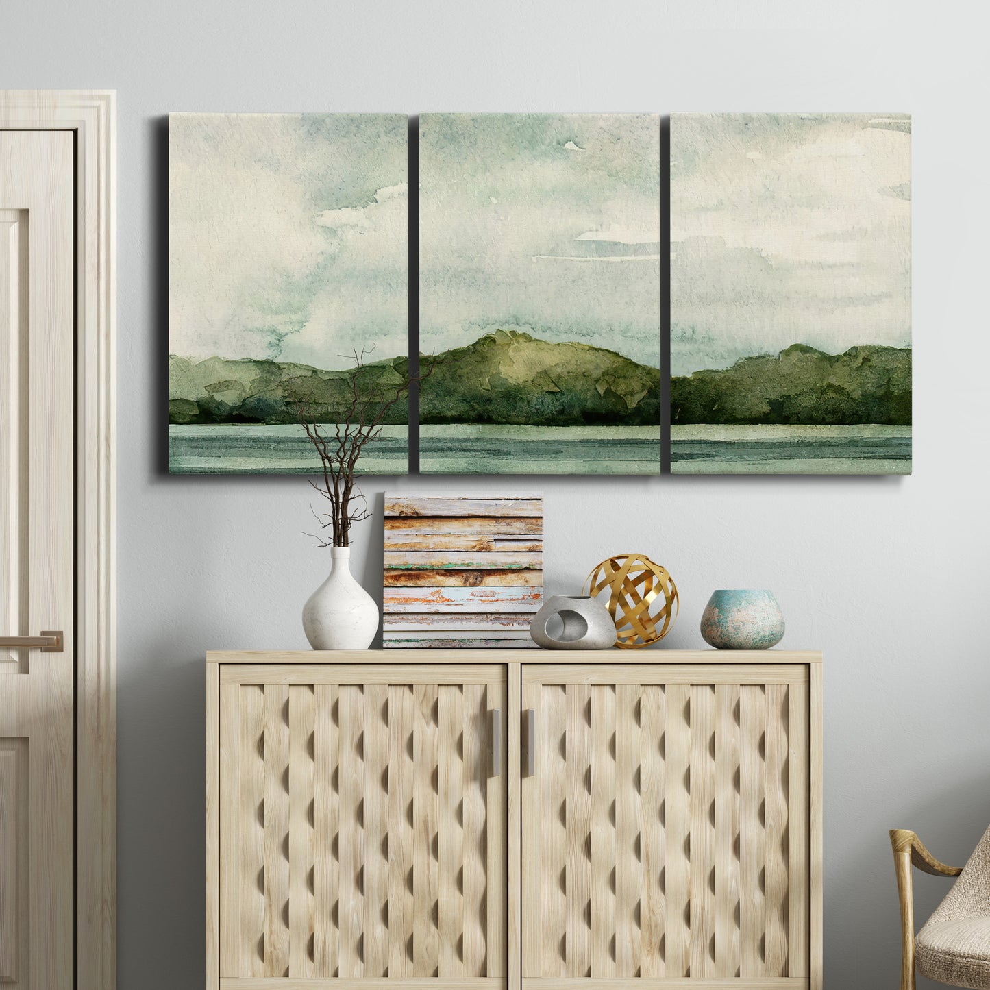 Three-panel canvas wall art featuring riverbank watercolor landscape, displayed above a cabinet in an entryway.