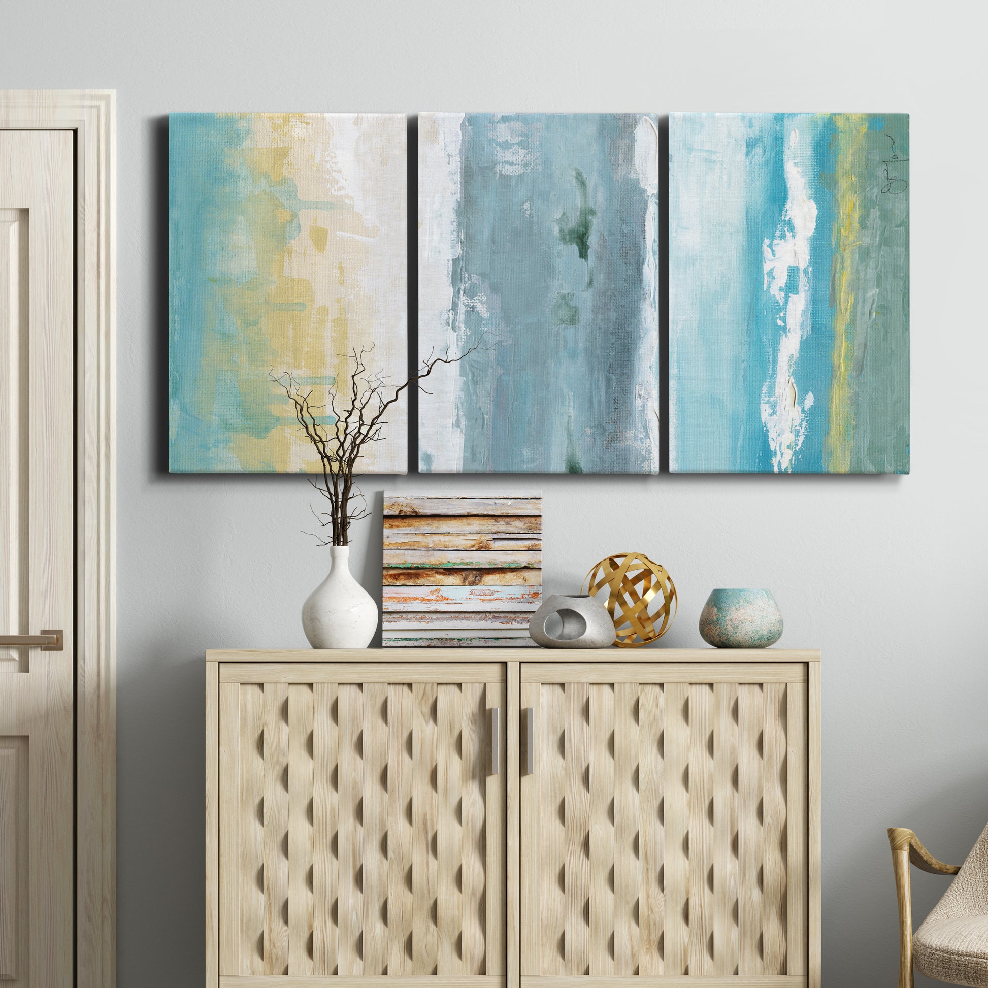Three-panel canvas wall art featuring abstract coastal shoreline textures, displayed above a cabinet in an entryway.