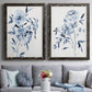 Set of two black barnwood framed canvas prints depicting paired expressive watercolor botanical paintings with indigo blossoms, gestural blue leaves, and airy white space above a sofa in a contemporary living room.