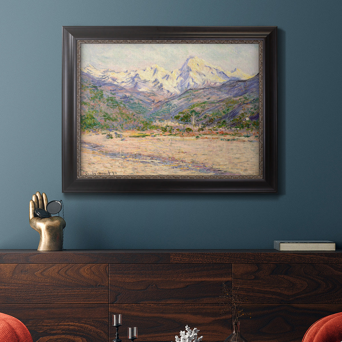 Impressionist valley landscape in southern France by Claude Monet in an ornate black frame with gilded inner detail displayed in a dark-toned interior setting.