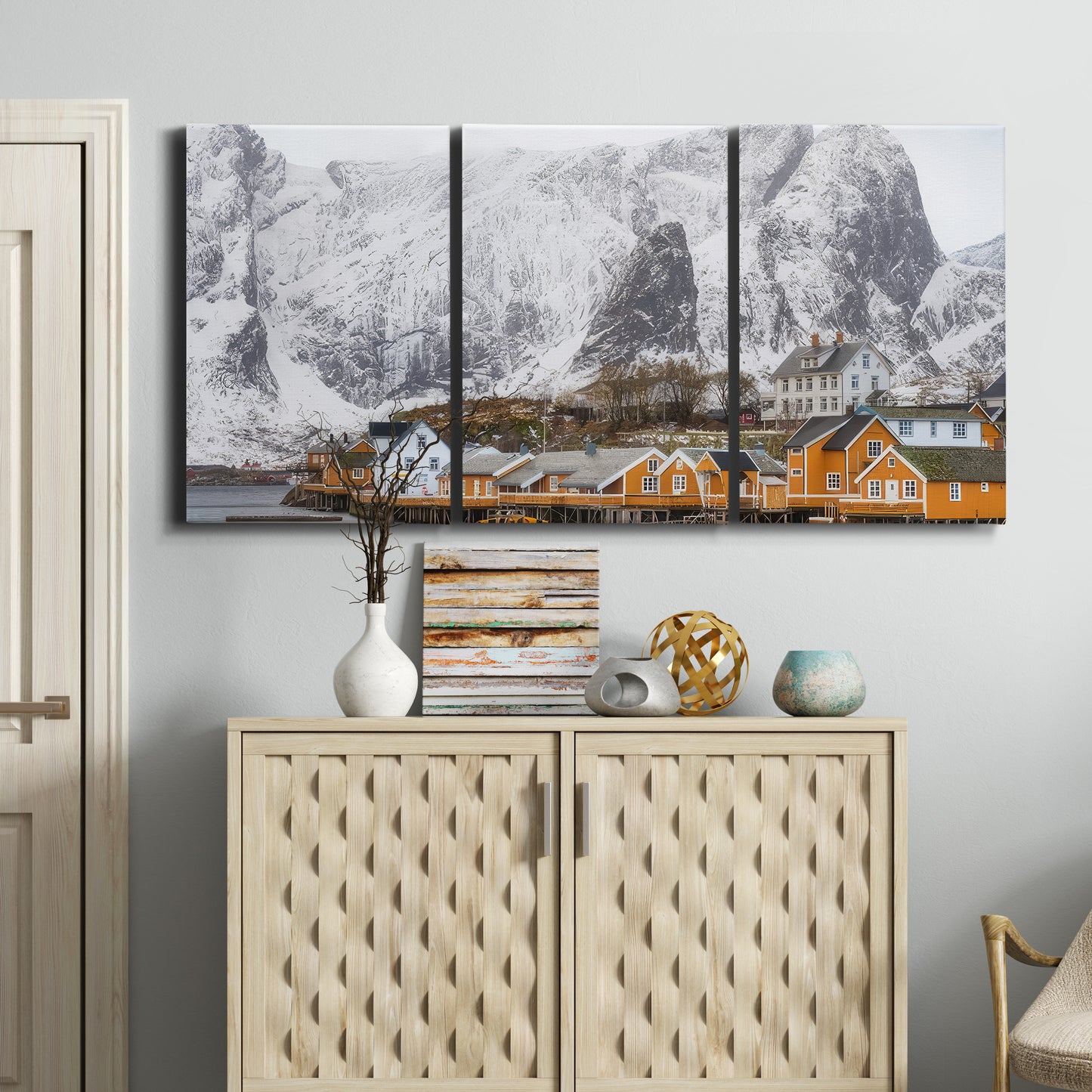 Three-panel canvas wall art featuring winter village street photography, displayed above a cabinet in an entryway.