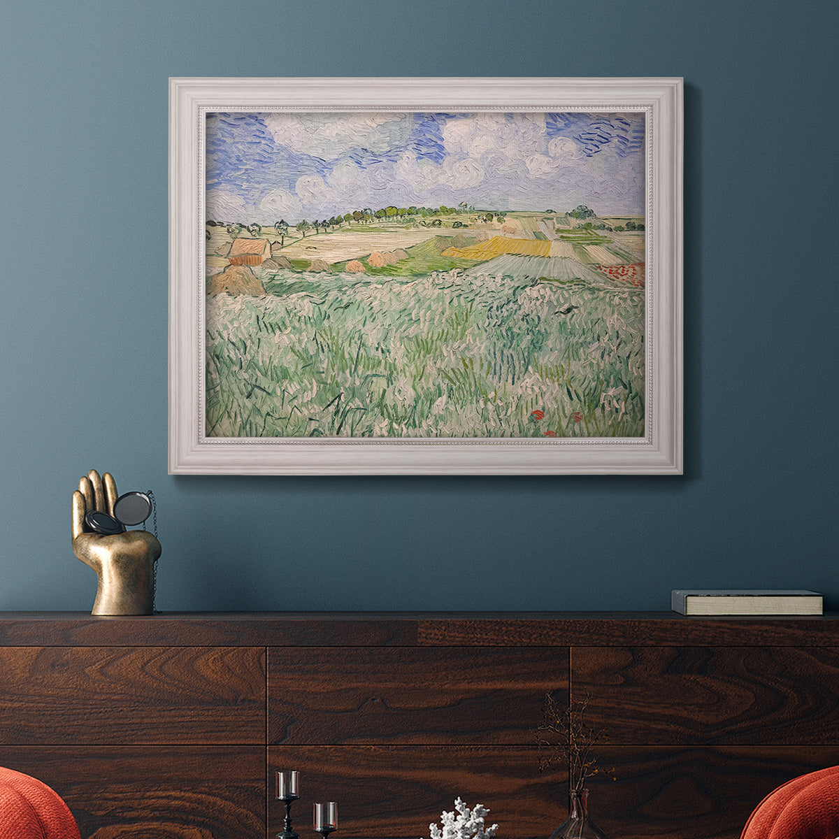 Impressionist countryside landscape near Auvers by Vincent van Gogh in an ornate weathered white frame displayed in a dark-toned interior setting.