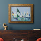 Coastal harbor watercolor painting in an ornate vintage gold frame displayed in a dark-toned interior setting.