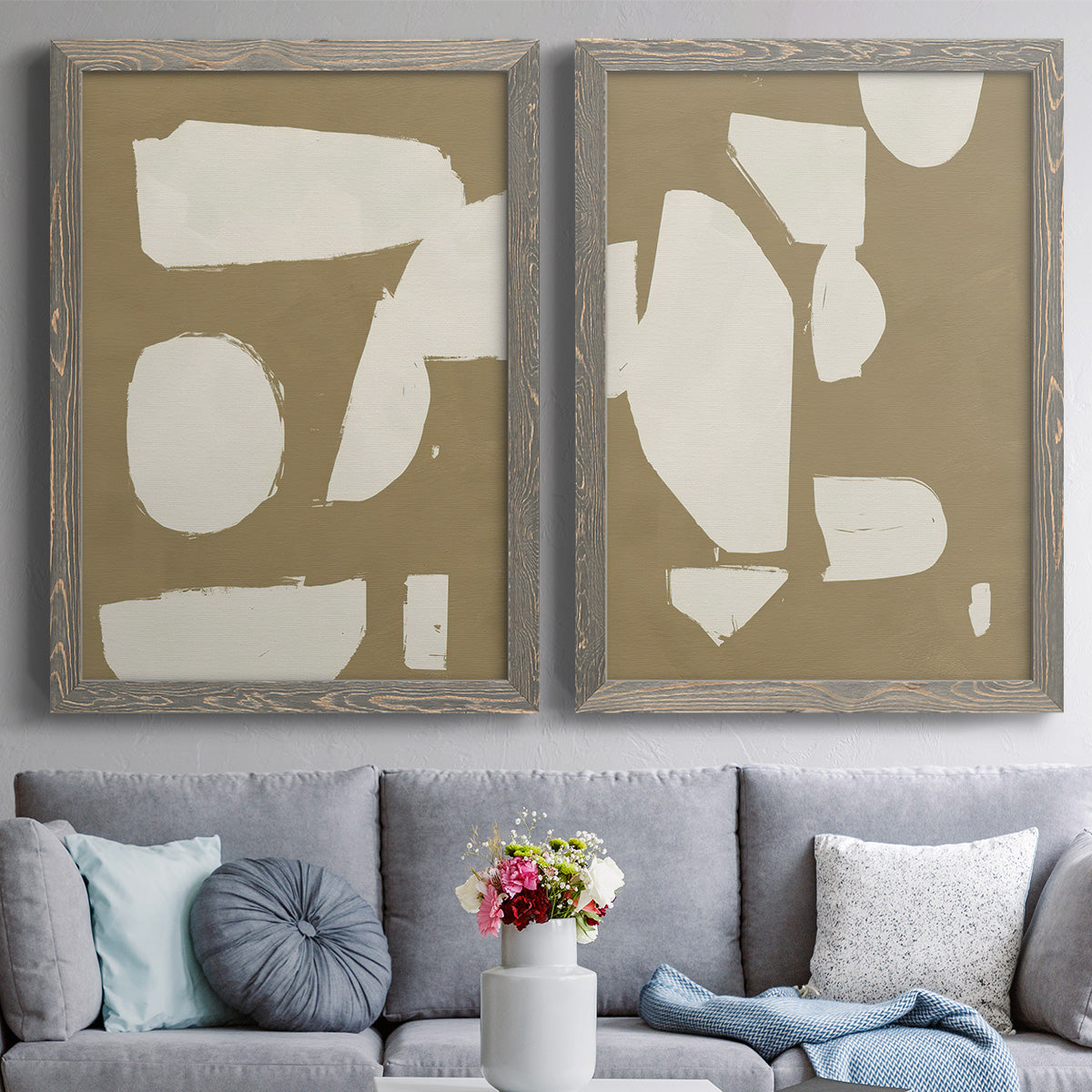 Set of two gray barnwood framed canvas prints depicting paired bold minimalist shape abstracts with flat blocky forms, rough painted edges, and strong negative space above a sofa in a contemporary living room.