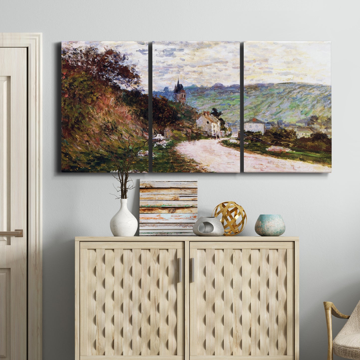 Three-panel canvas wall art featuring country road through village, displayed above a cabinet in an entryway.