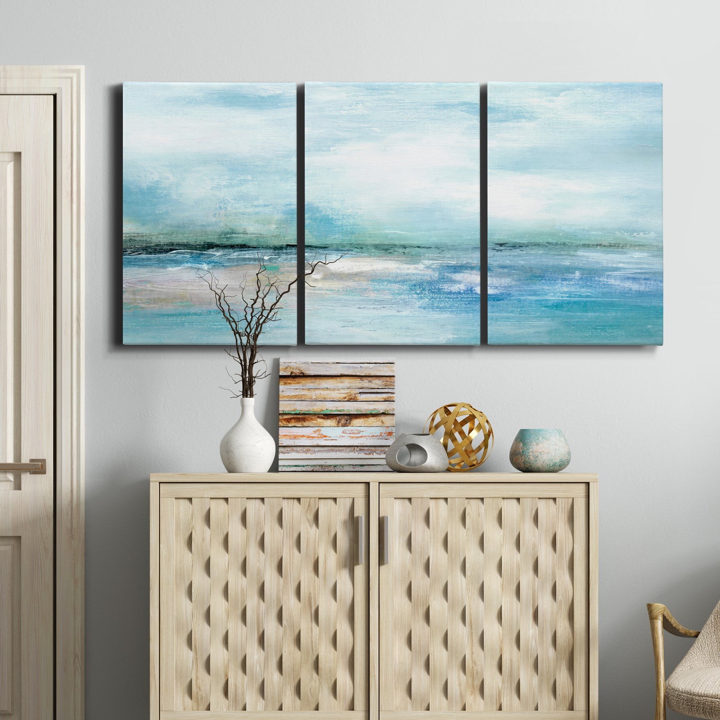 Three-panel canvas wall art featuring sunset silhouette over coastal water, displayed above a cabinet in an entryway.
