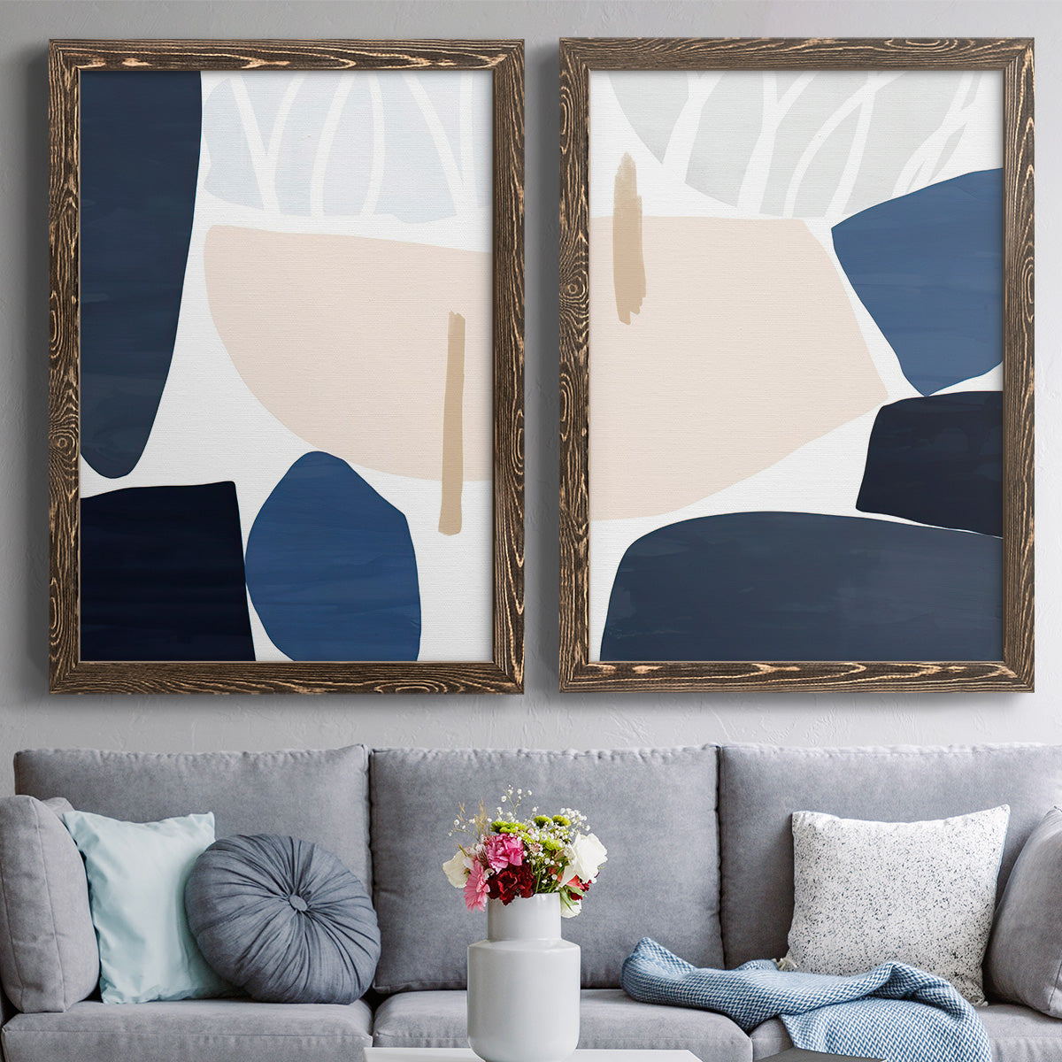 Set of two walnut barnwood framed canvas prints depicting paired minimalist color-block abstracts with rounded dark forms, pale sand fields, and clean modern edges above a sofa in a contemporary living room.