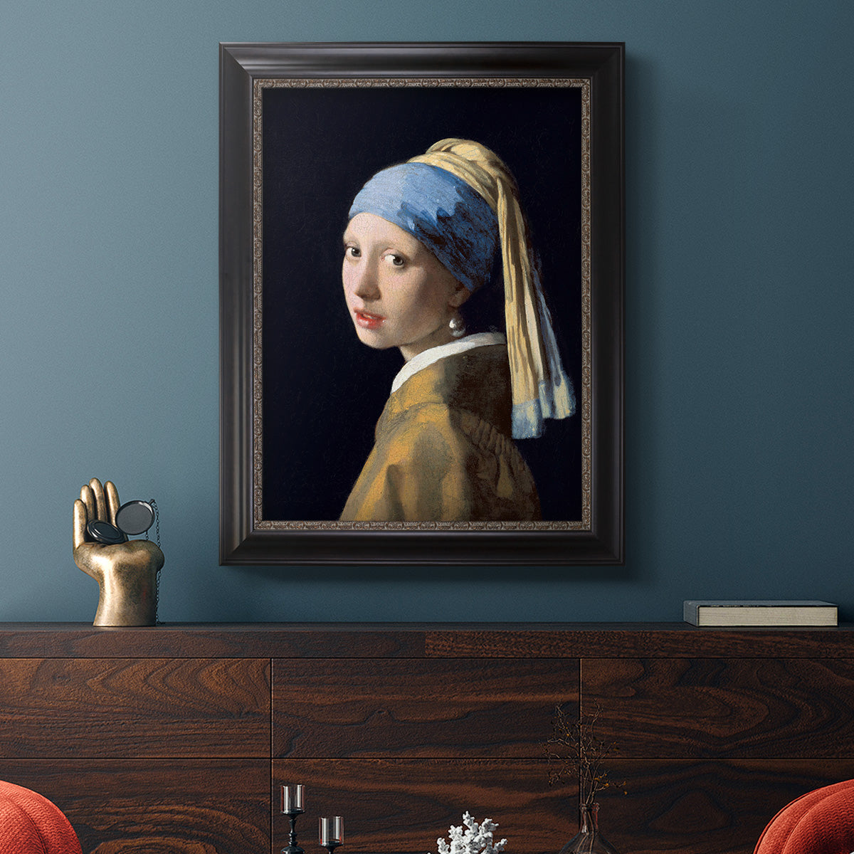 Iconic portrait of a girl wearing a pearl earring by Johannes Vermeer in an ornate black frame with gilded inner detail displayed in a dark-toned interior setting.