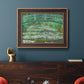 Impressionist garden scene with Japanese bridge and water lilies by Claude Monet in an ornate bronzed mahogany wood frame displayed in a dark-toned interior setting.