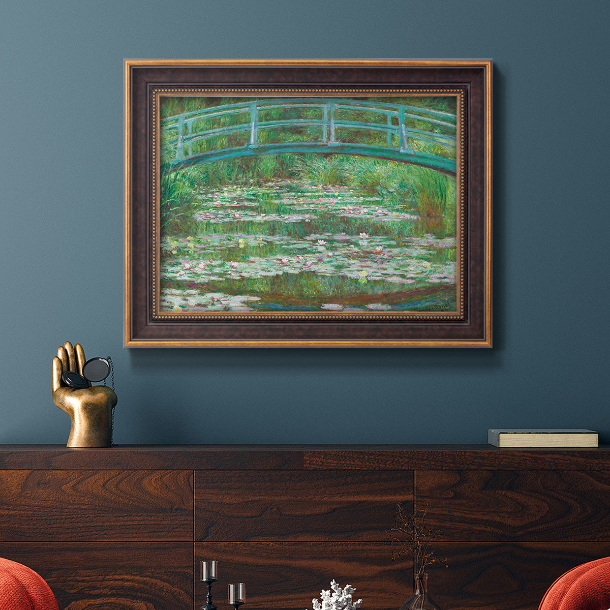 Impressionist garden scene with Japanese bridge and water lilies by Claude Monet in an ornate bronzed mahogany wood frame displayed in a dark-toned interior setting.