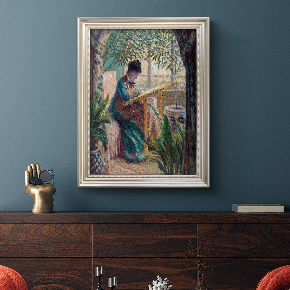 Impressionist portrait of Madame Monet sewing by Claude Monet in an ornate champagne frame displayed in a dark-toned interior setting.