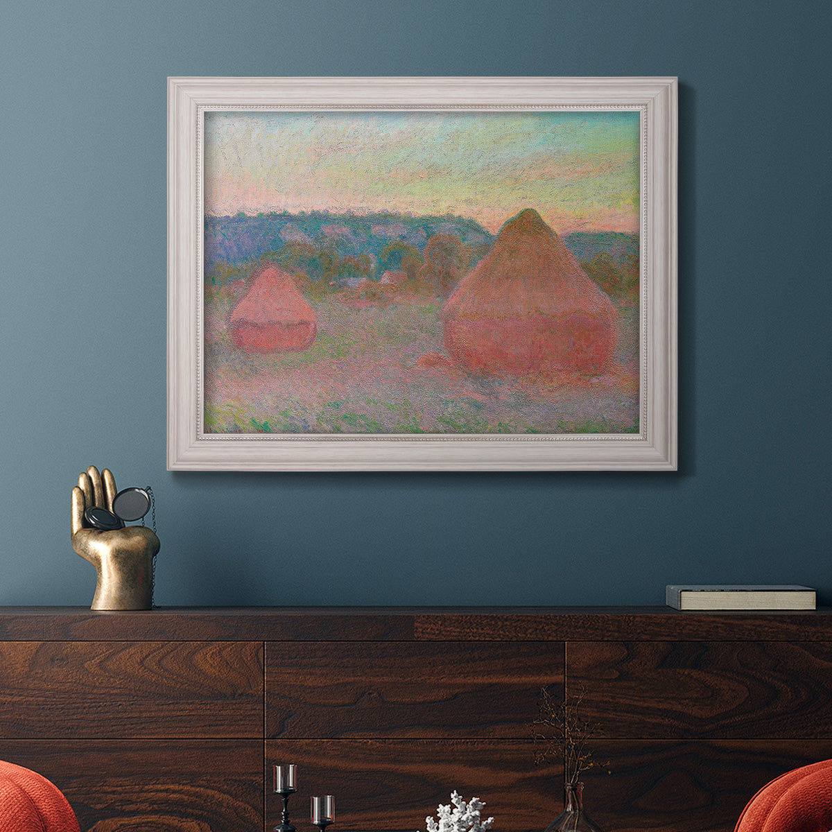 Impressionist haystack series landscape by Claude Monet in an ornate weathered white frame displayed in a dark-toned interior setting.