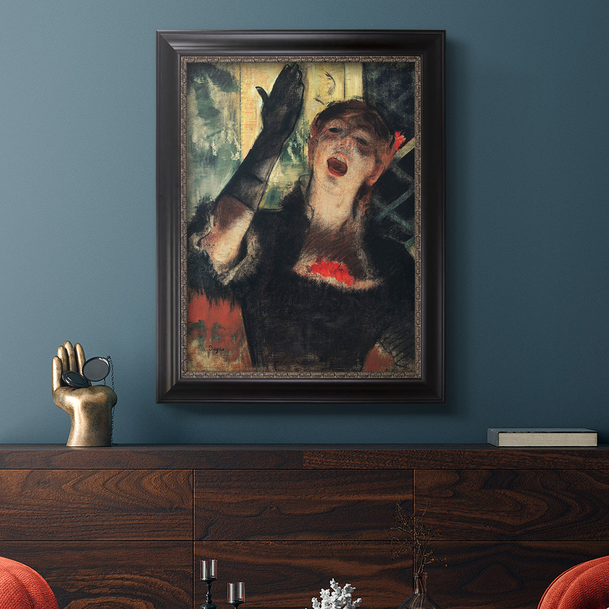 Impressionist portrait of a café singer by Edgar Degas in an ornate black frame with gilded inner detail displayed in a dark-toned interior setting.