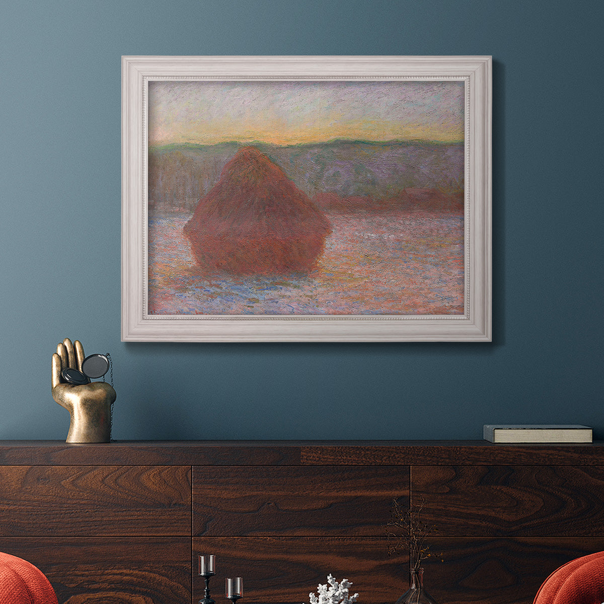 Impressionist haystack sunset scene in winter by Claude Monet in an ornate weathered white frame displayed in a dark-toned interior setting.