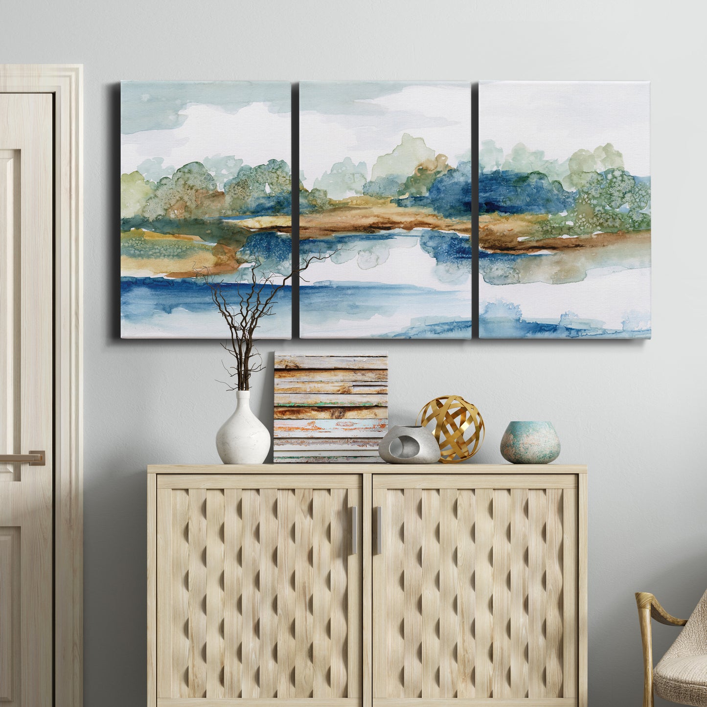Three-panel canvas wall art featuring abstract blue watercolor landscape, displayed above a cabinet in an entryway.