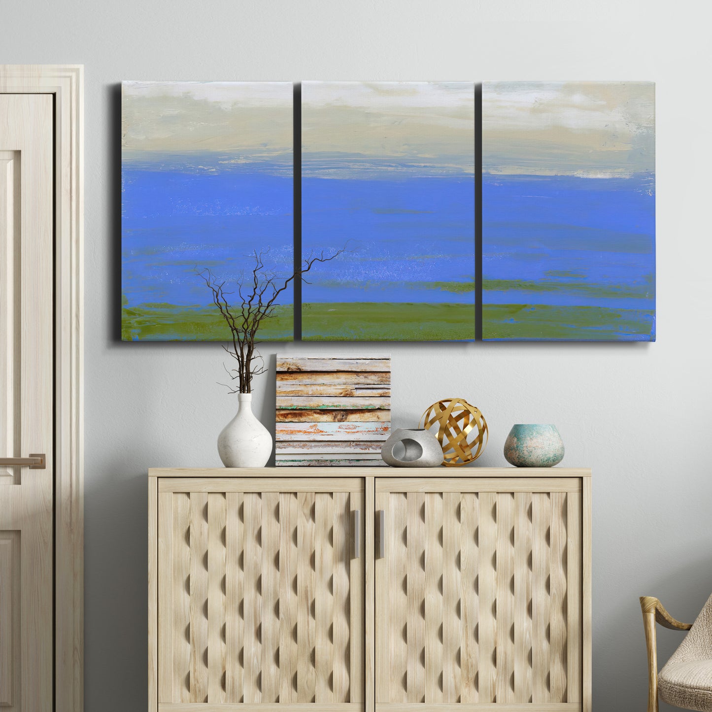 Three-panel canvas wall art featuring abstract coastal inlet landscape, displayed above a cabinet in an entryway.
