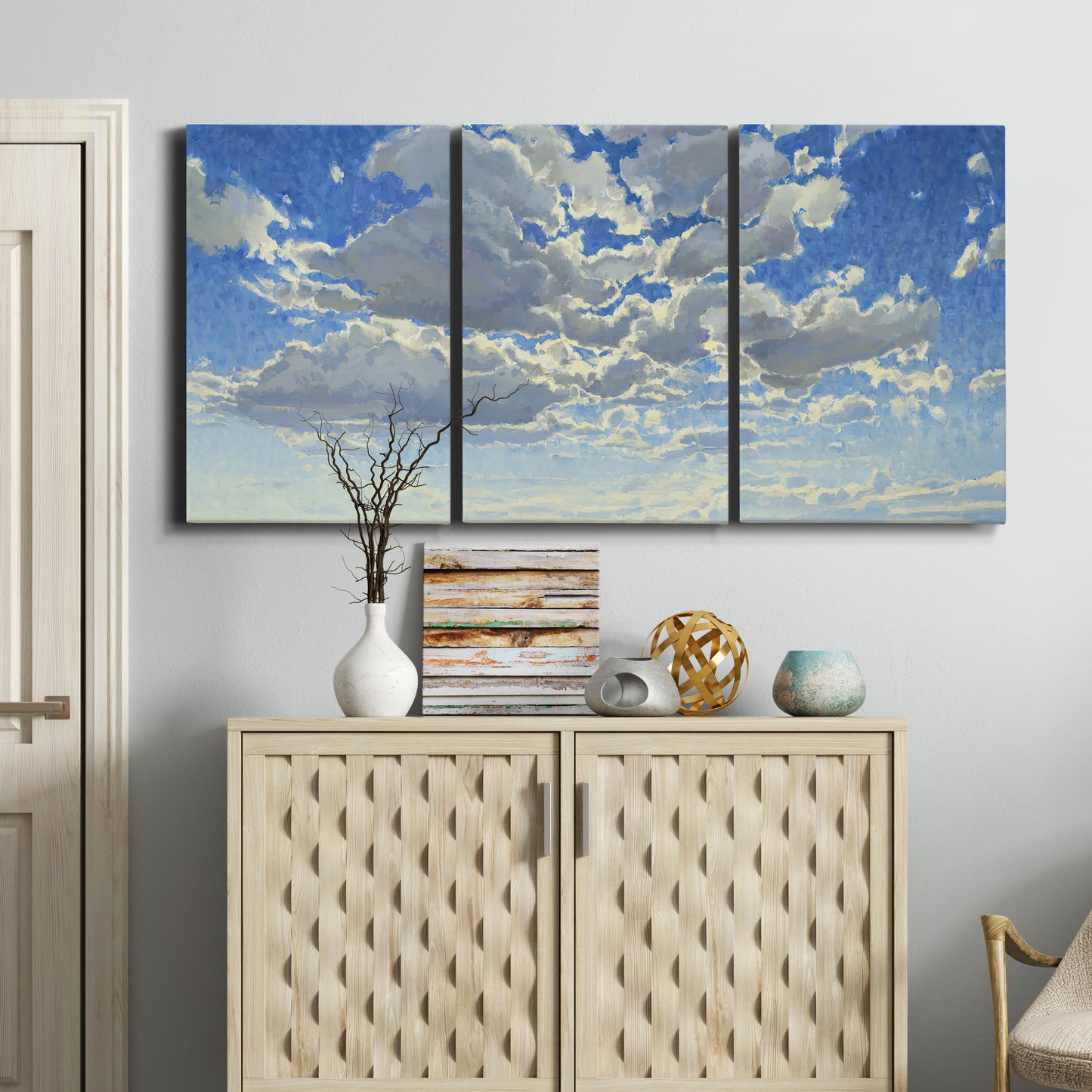 Three-panel canvas wall art featuring whimsical cloud filled sky landscape, displayed above a cabinet in an entryway.