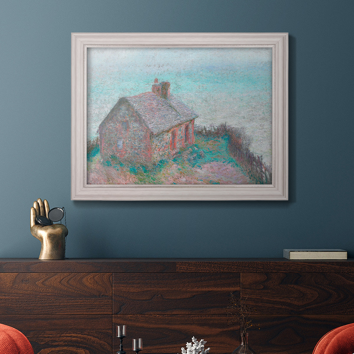 Impressionist coastal building landscape by Claude Monet in an ornate weathered white frame displayed in a dark-toned interior setting.