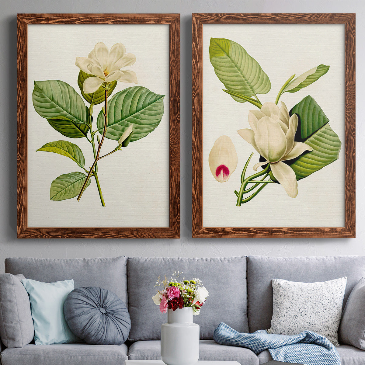 Set of two maple barnwood framed canvas prints depicting paired traditional botanical paintings with large pale petals, leafy branches, and soft watercolor shading above a sofa in a contemporary living room.