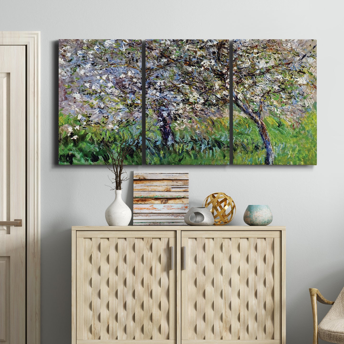 Three-panel canvas wall art featuring apple trees blooming beside water, displayed above a cabinet in an entryway.