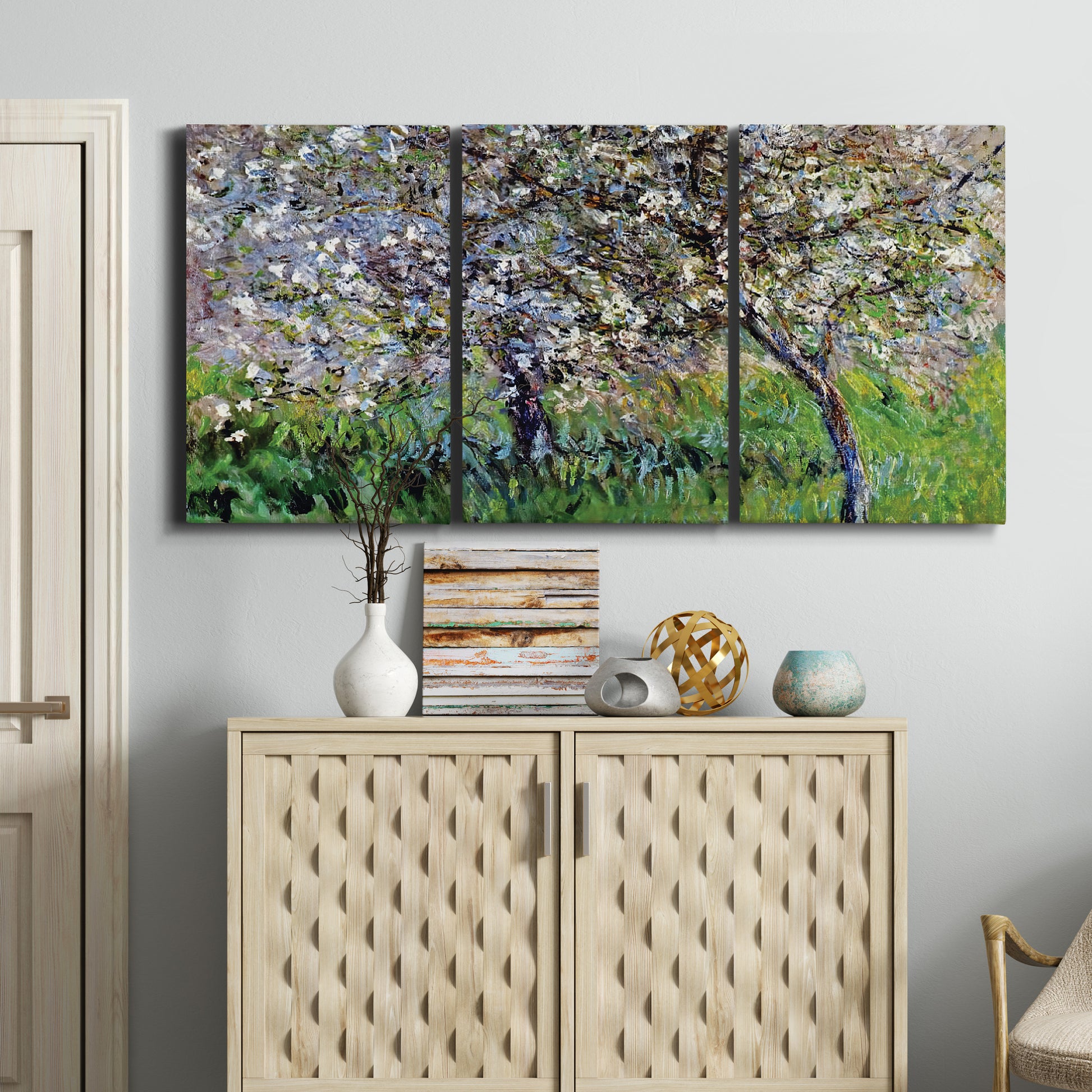 Three-panel canvas wall art featuring apple trees blooming beside water, displayed above a cabinet in an entryway.