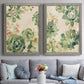 Set of two gray barnwood framed canvas prints depicting paired decorative botanical pattern prints with green rosettes, peach blossoms, and mosaic-like outlines above a sofa in a contemporary living room.