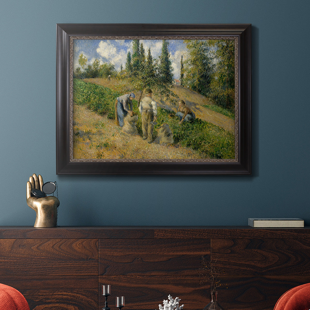 Impressionist countryside harvest scene by Camille Pissarro in an ornate black frame with gilded inner detail displayed in a dark-toned interior setting.