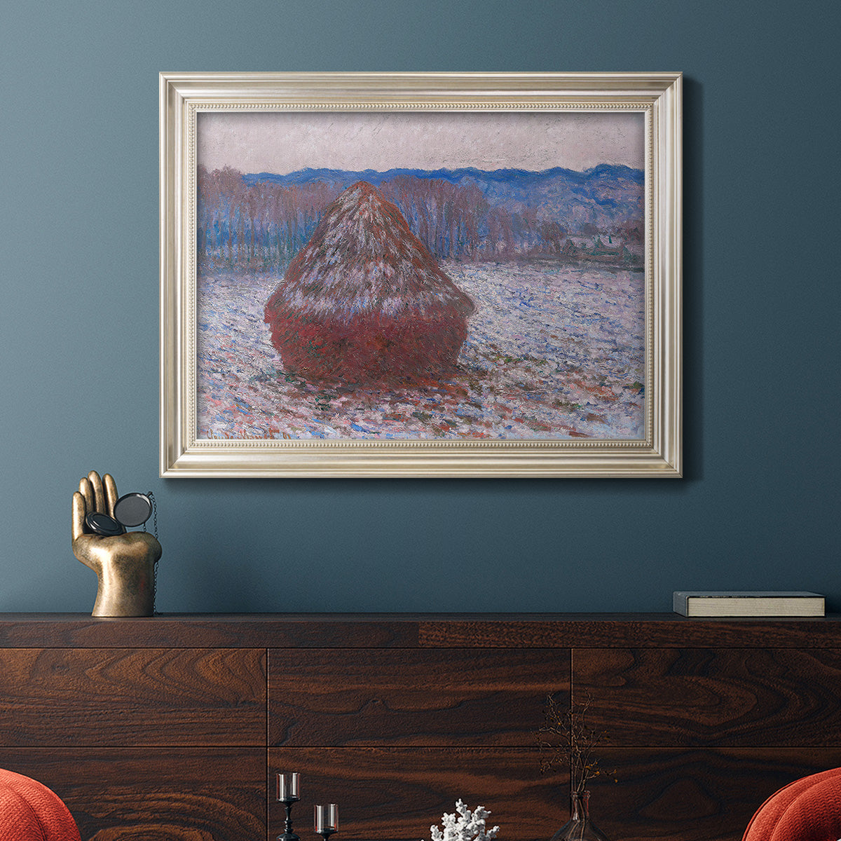 Impressionist single haystack landscape by Claude Monet in an ornate champagne frame displayed in a dark-toned interior setting.