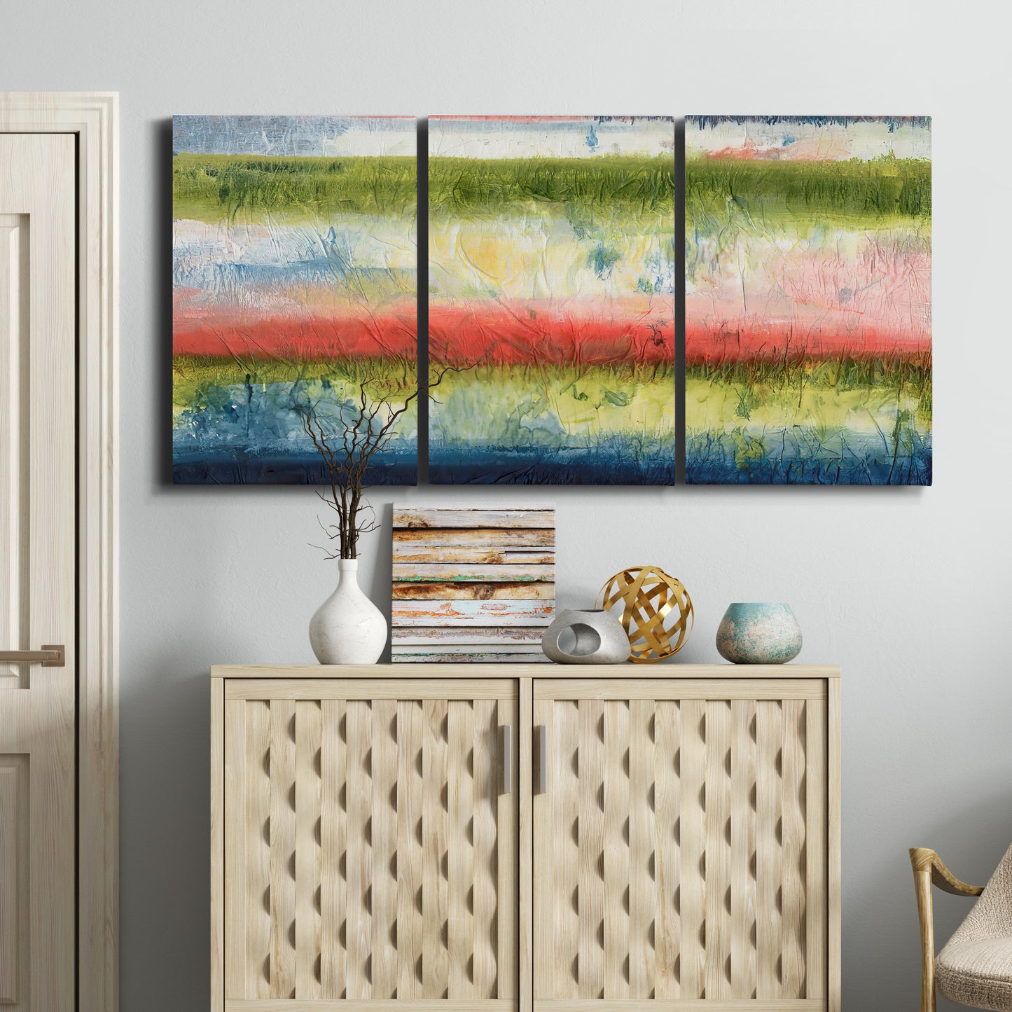 Three-panel canvas wall art featuring layered abstract color banding, displayed above a cabinet in an entryway.
