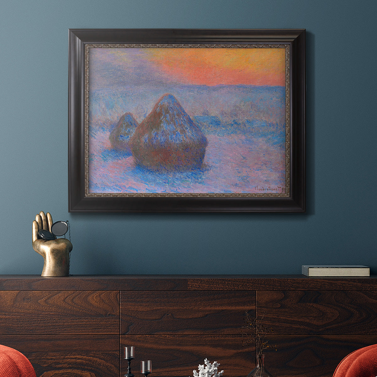 Impressionist haystack scene at sunset by Claude Monet in an ornate black frame with gilded inner detail displayed in a dark-toned interior setting.