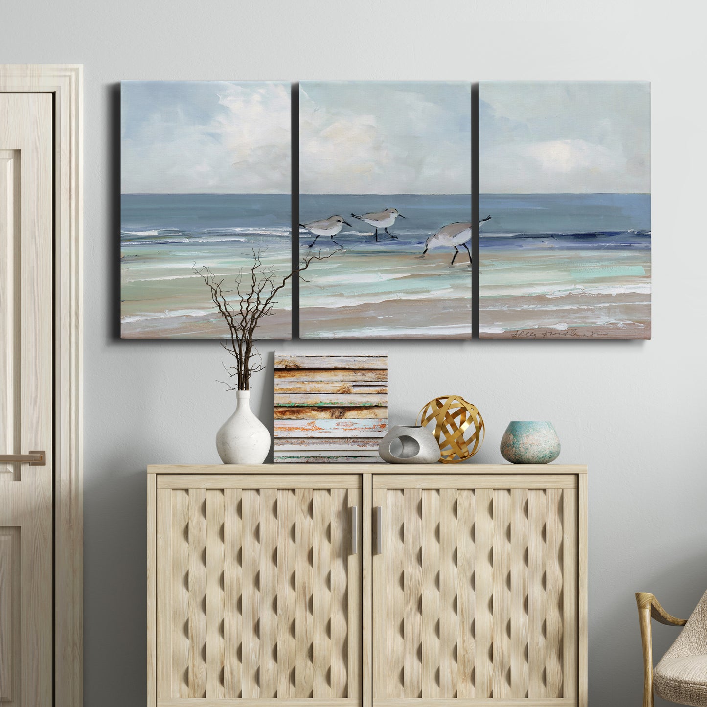 Three-panel canvas wall art featuring shore birds searching along beach, displayed above a cabinet in an entryway.