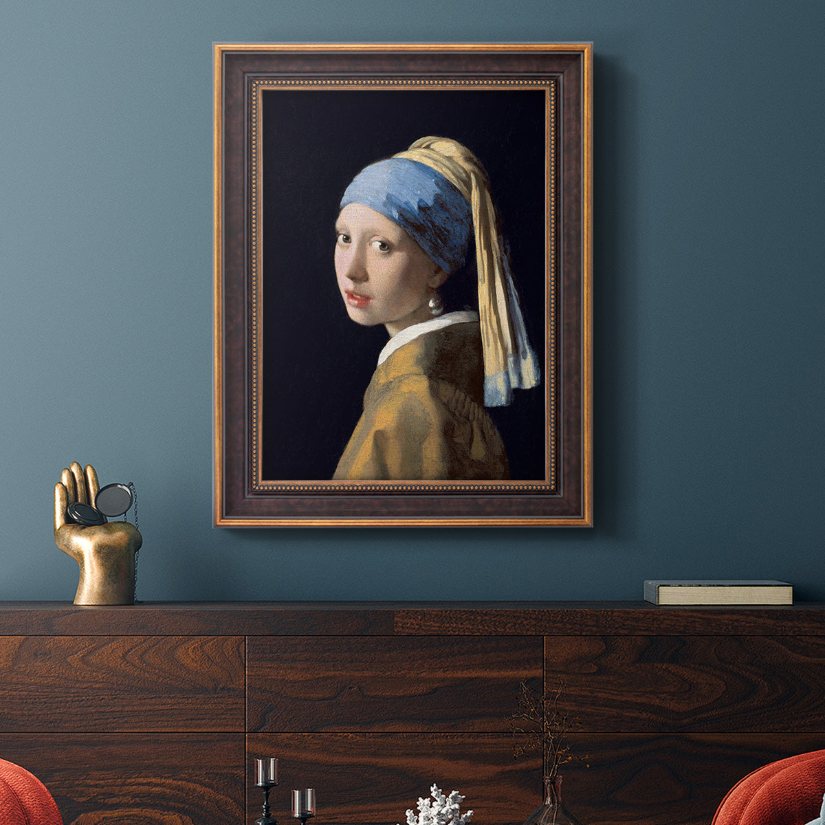 Iconic portrait of a girl wearing a pearl earring by Johannes Vermeer in an ornate bronzed mahogany wood frame displayed in a dark-toned interior setting.