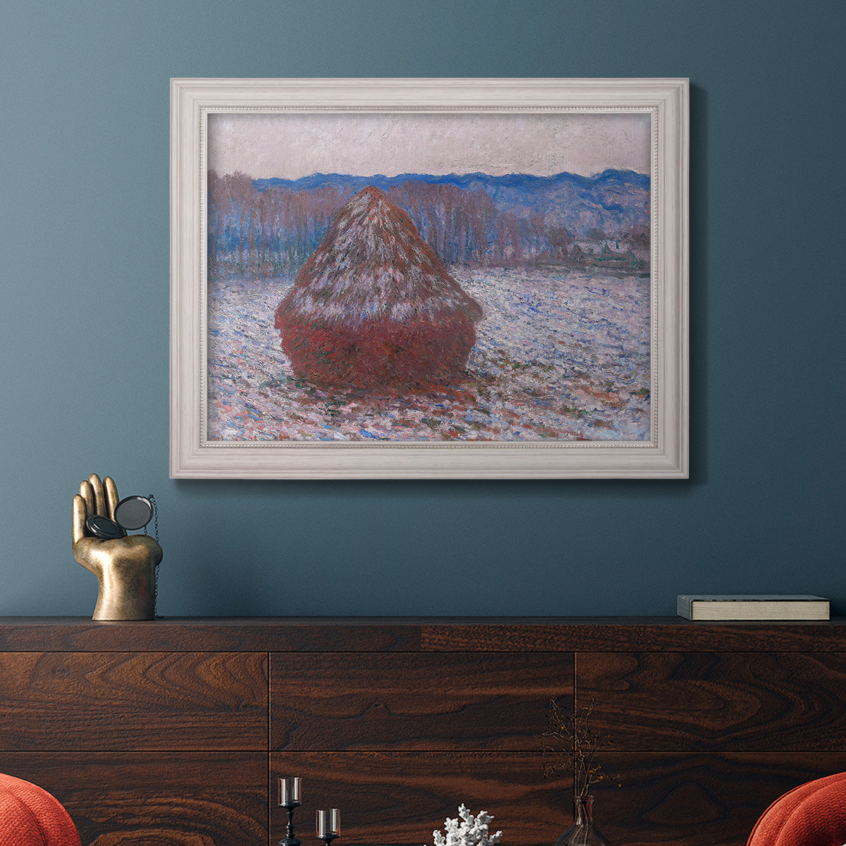 Impressionist single haystack landscape by Claude Monet in an ornate weathered white frame displayed in a dark-toned interior setting.