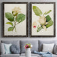 Set of two black barnwood framed canvas prints depicting paired traditional botanical paintings with large pale petals, leafy branches, and soft watercolor shading above a sofa in a contemporary living room.