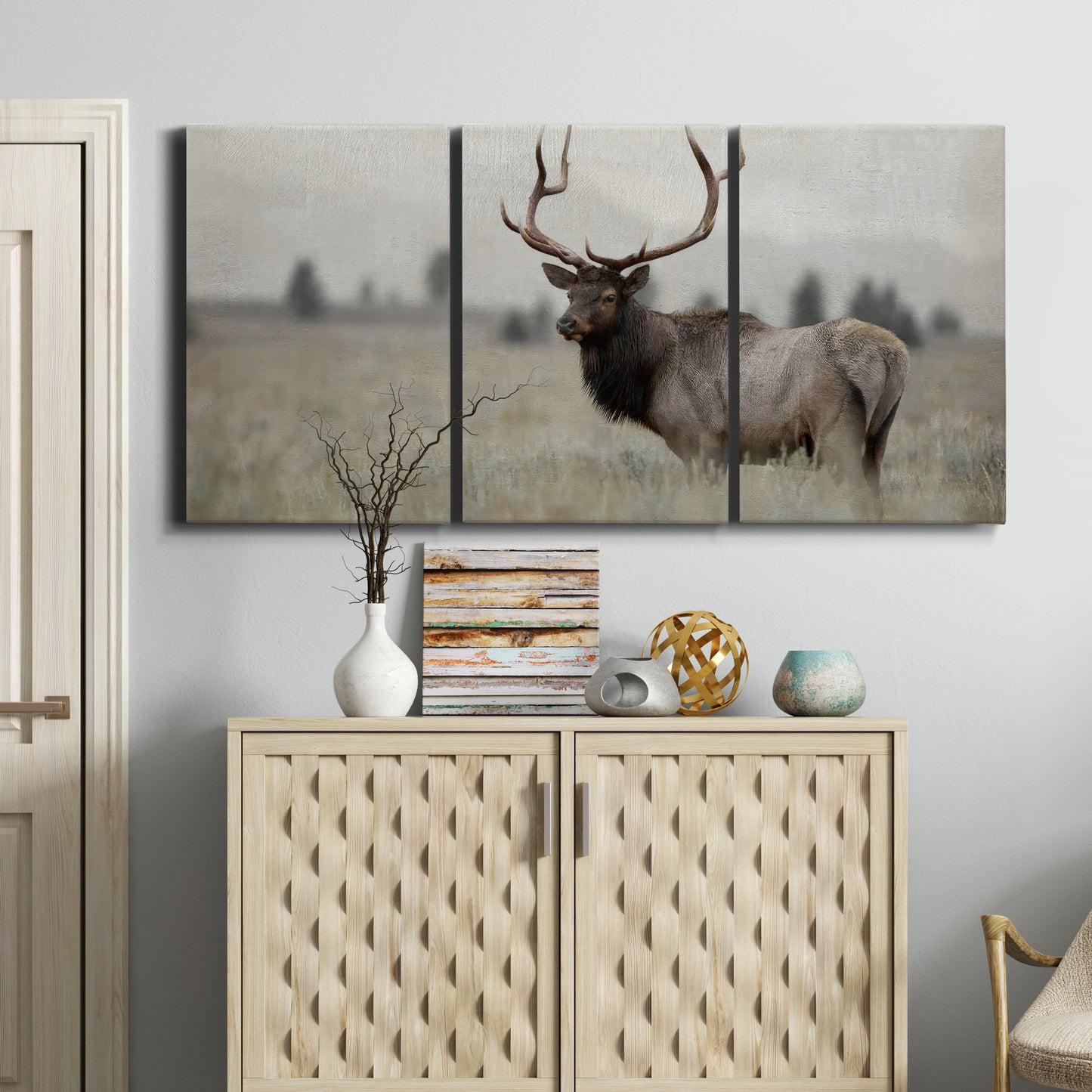 Three-panel canvas wall art featuring elk standing in open grassland, displayed above a cabinet in an entryway.