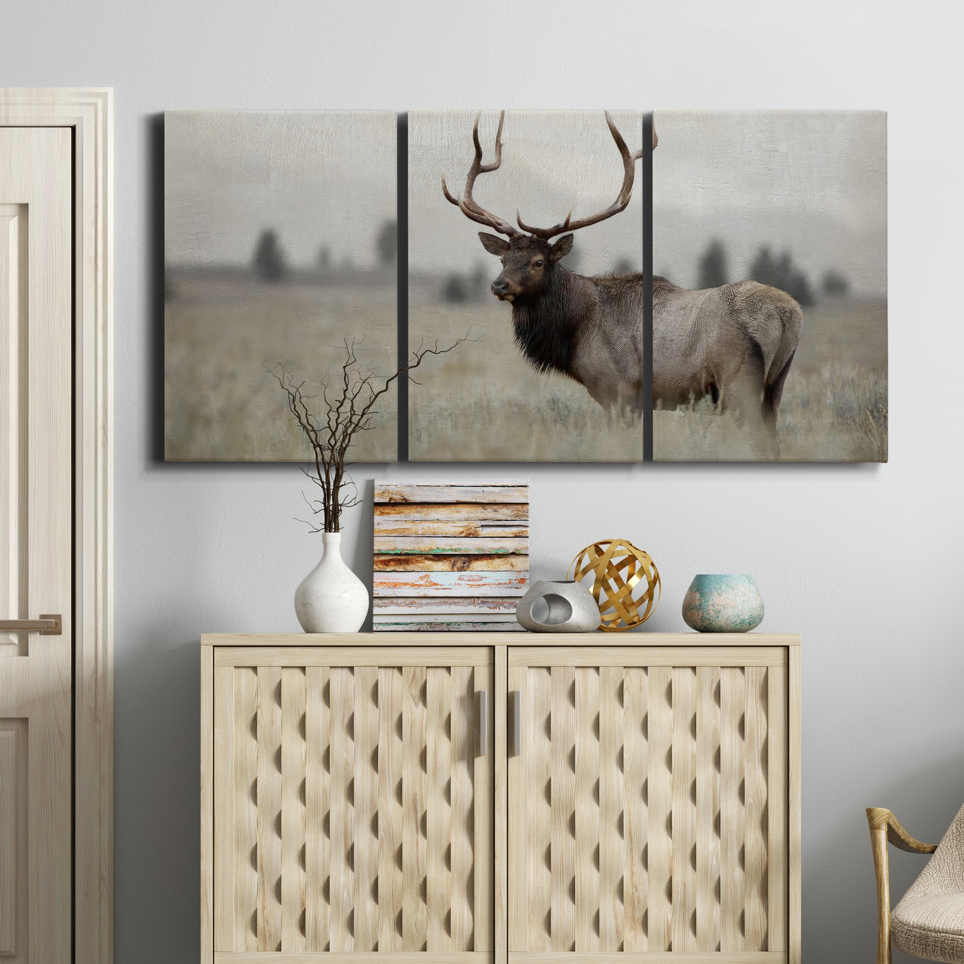 Three-panel canvas wall art featuring elk standing in open grassland, displayed above a cabinet in an entryway.