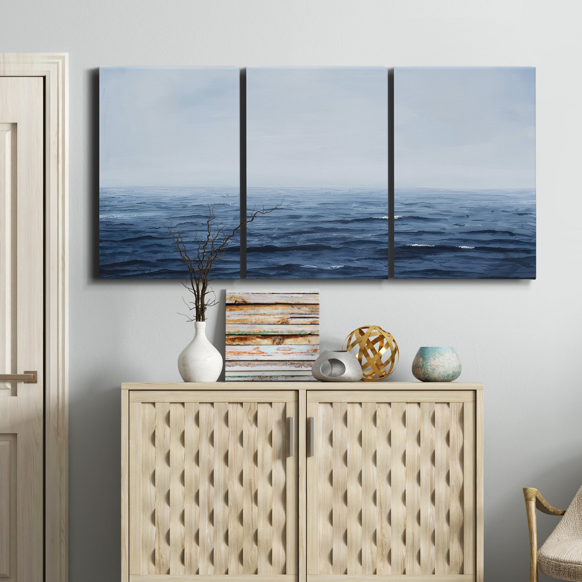 Three-panel canvas wall art featuring grayscale seascape with horizon, displayed above a cabinet in an entryway.