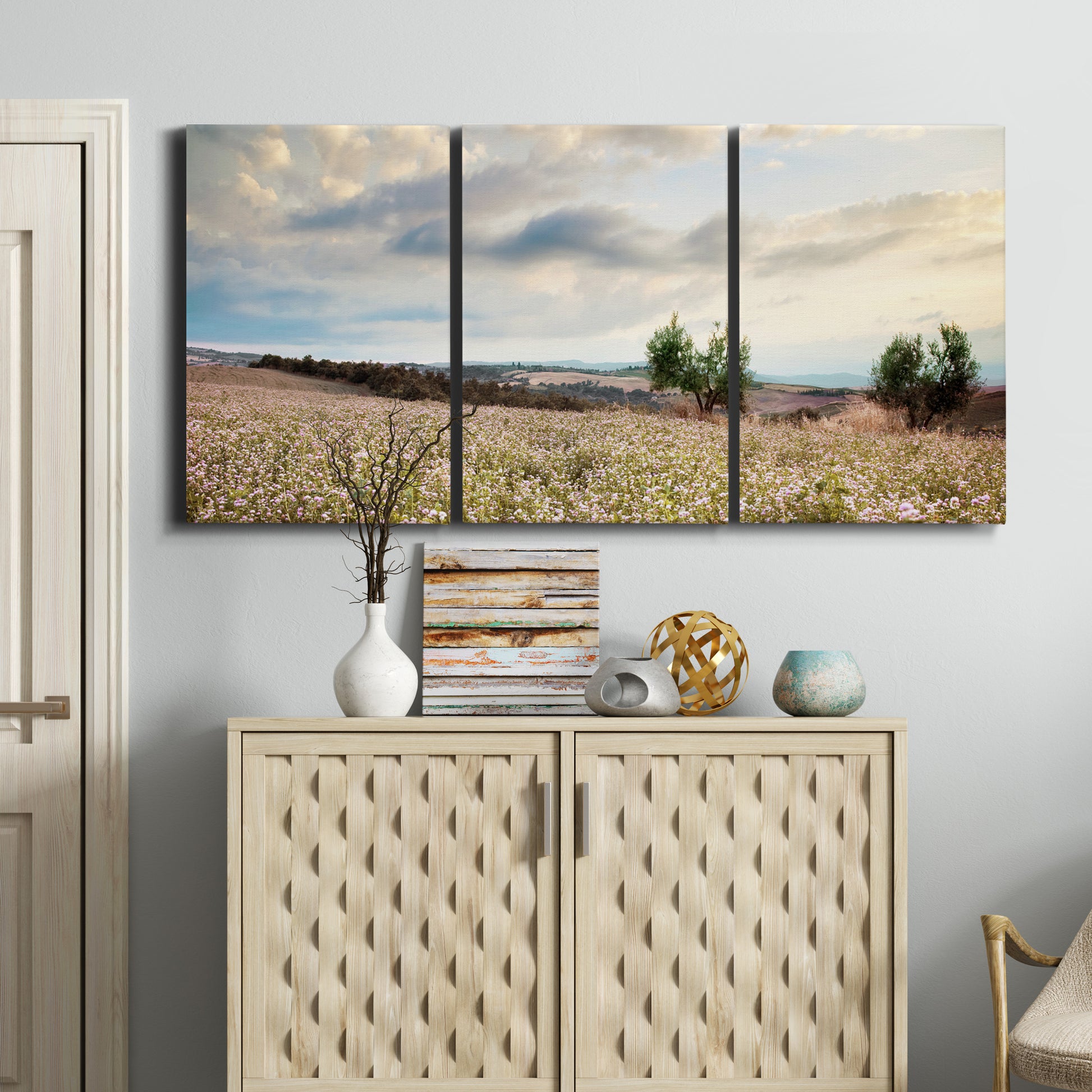 Three-panel canvas wall art featuring wildflowers across tuscan landscape, displayed above a cabinet in an entryway.