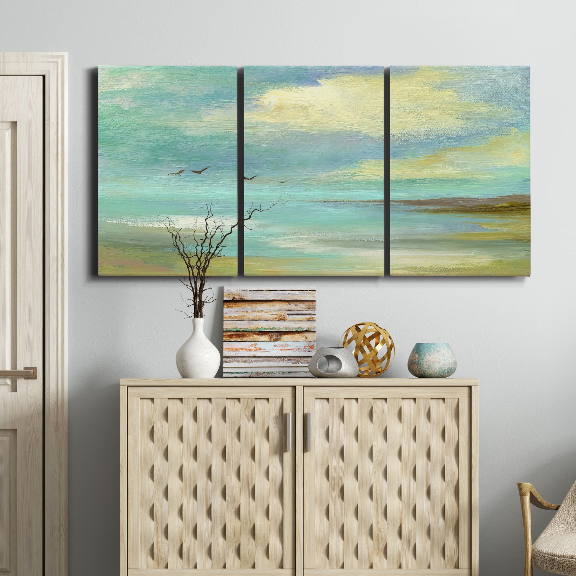 Three-panel canvas wall art featuring calm coastal drift patterns, displayed above a cabinet in an entryway.
