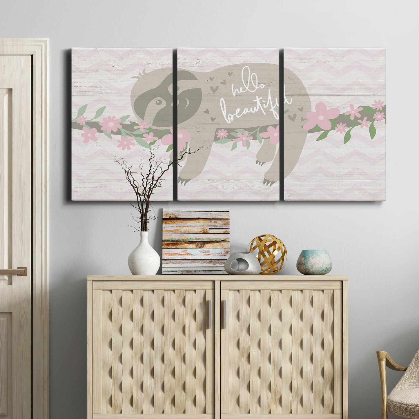 Three-panel canvas wall art featuring sloth with floral decorative elements, displayed above a cabinet in an entryway.