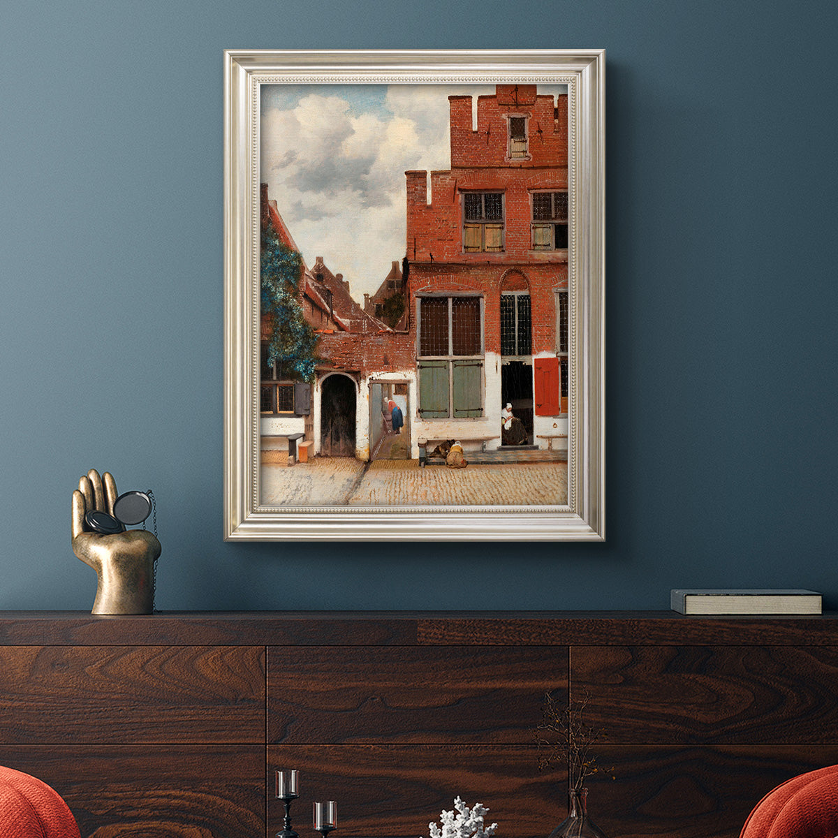 Realist city street scene by Johannes Vermeer in an ornate champagne frame displayed in a dark-toned interior setting.