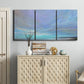 Three-panel canvas wall art featuring coastal shoreline with gentle surf, displayed above a cabinet in an entryway.
