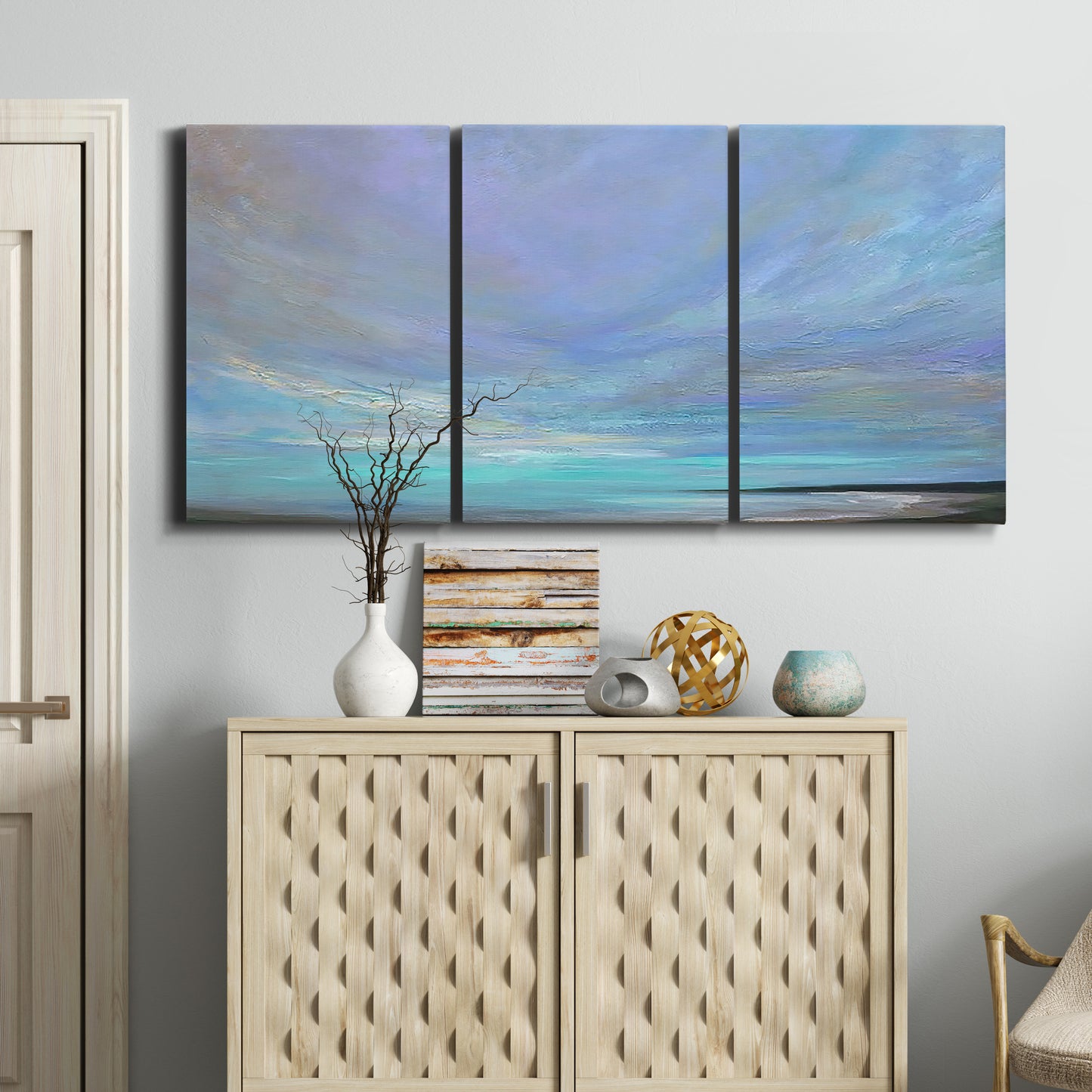 Three-panel canvas wall art featuring coastal shoreline with gentle surf, displayed above a cabinet in an entryway.