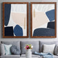 Set of two maple barnwood framed canvas prints depicting paired minimalist color-block abstracts with rounded dark forms, pale sand fields, and clean modern edges above a sofa in a contemporary living room.